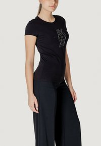 T-shirt nera a maniche corte con un design grafico testurizzato sul davanti, abbinata a pantaloni neri a gamba larga.