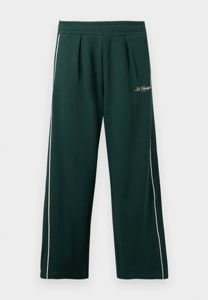 Pantalon large vert foncé avec ceinture élastique, liseré blanc sur le côté, plis à l'avant et petit texte blanc brodé sur la cuisse supérieure.
