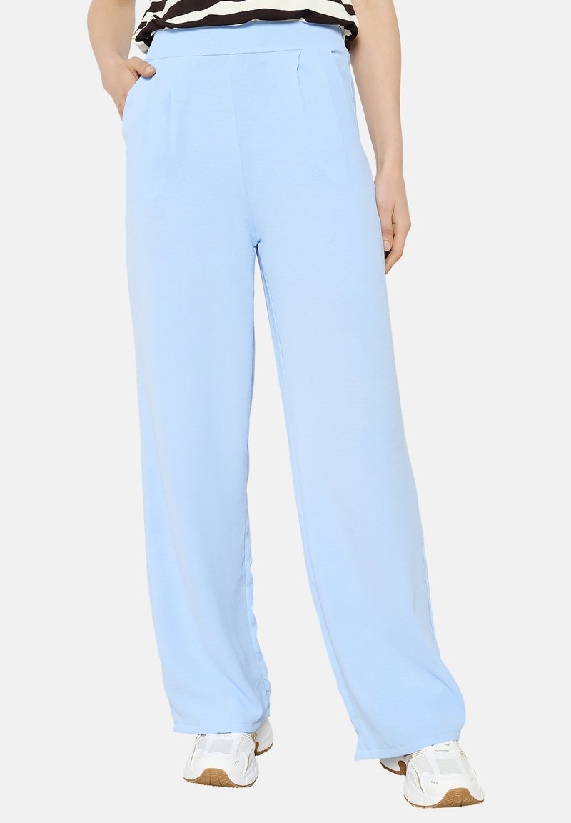 Pantalones de pierna ancha en azul claro, con una textura suave, que presentan pliegues frontales y una cintura alta. Combinados con sneakers blancos.