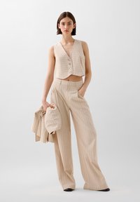 Beige cropped vest met knoopsluiting en verticale strepen, gecombineerd met bijpassende wijde broek met zijzakken en een gestructureerde stof.