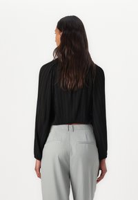 Blusa nera plissettata a maniche lunghe con un design cropped, abbinata a pantaloni grigi chiari a righe sottili, che mettono in evidenza una texture liscia e una silhouette aderente.