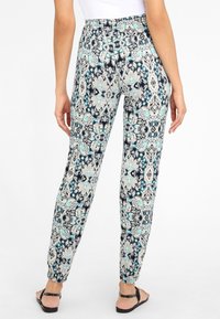 Elastīgas jostas bikses ar rakstainu dizainu tumši zilā, krēmkrāsas un teal krāsā, ar sašaurinātu kāju un elastīgiem aizdariem pie potītēm.