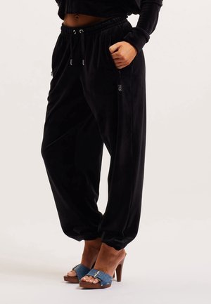 Persoon draagt zwarte velours joggers met elastische boorden en een taille met trekkoord, gecombineerd met blauwe denim sandalen met open teen en hoge hak.