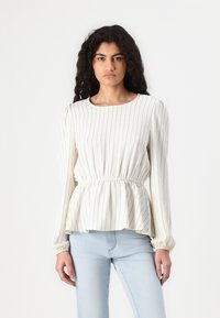 Blouse peplum blanche à rayures, à manches longues, avec une taille élastique et un tissu doux. Associée à un jean bleu clair.