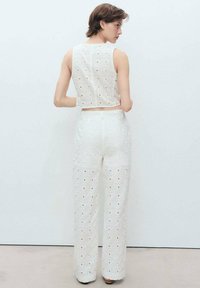 Witte crop top en wijde broek met een textuurpatroon en uitsparingen. De stof is lichtgewicht en iets doorzichtig.