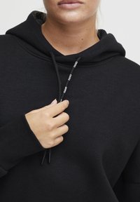 Felpa nera con cappuccio realizzata in tessuto morbido, presenta un cordoncino con dettagli di marca. Il design include un colletto alto e polsini a costine.