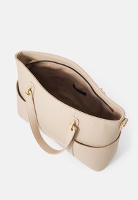 Beige syntetisk håndtaske med en tekstureret overflade, dobbelte håndtag, guldhardware og et rummeligt, uforet interiør med en lynlås til lukning.