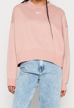 Rosa kortärmad sweatshirt med rund hals och långa ärmar. Har en liten vit Nike-logotyp på bröstet. Kombinerad med blekta blåjeans.