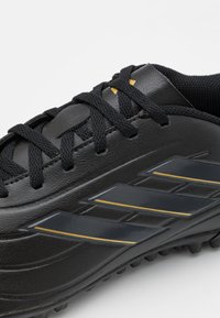 Zapatilla deportiva negra con parte superior de cuero liso, cordones negros, tres rayas brillantes en gris oscuro y suela texturizada para un mejor agarre.
