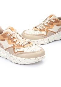 Zapatillas con parte superior de cuero crema perforado, acentos de ante marrón y cordones dorados. Suela gruesa blanca con detalles moteados.