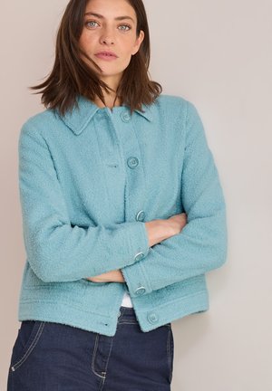 Veste texturée bleu clair avec col, boutons à l'avant et deux poches latérales. Design court et manches longues avec accents en bouton.