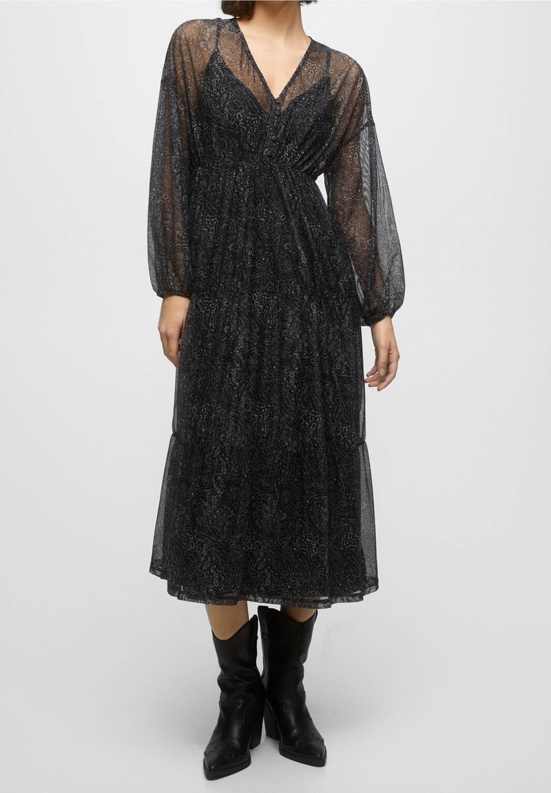 Robe noire midi avec de longues manches transparentes, motif paisley, taille froncée, ourlet en couches et décolleté en V, associée à des bottes noires montantes.