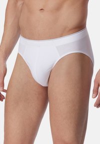 Weiße Baumwoll-Unterhosen mit glatter Oberfläche, die ein hoch geschnittenes Bein-Design und einen unterstützenden Bund aufweisen, präsentiert an einem männlichen Model.