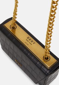 Borsa a mano in pelle nera con motivo trapuntato, tracolla a catena color oro e pannello rettangolare dorato con il logo DKNY.