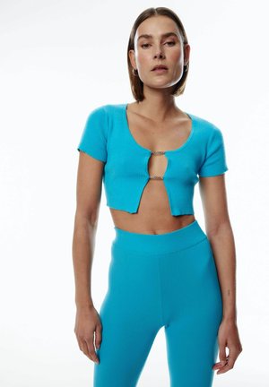 Turquoise geribbelde crop top met korte mouwen, voorzien van een opening aan de voorkant verbonden door een ketting. Gepaard met bijpassende geribbelde high-waisted legging.