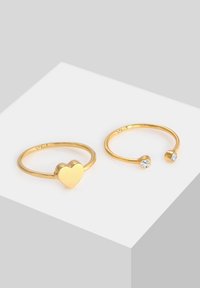 Due anelli d'oro: uno presenta una forma a cuore, l'altro ha una pietra trasparente singola all'estremità. Entrambi hanno una finitura liscia e lucida.