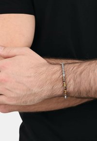 Bracciale in metallo caratterizzato da una combinazione di perle argentate e colorate con un design liscio e elegante. Indossato su un polso contro una t-shirt nera.