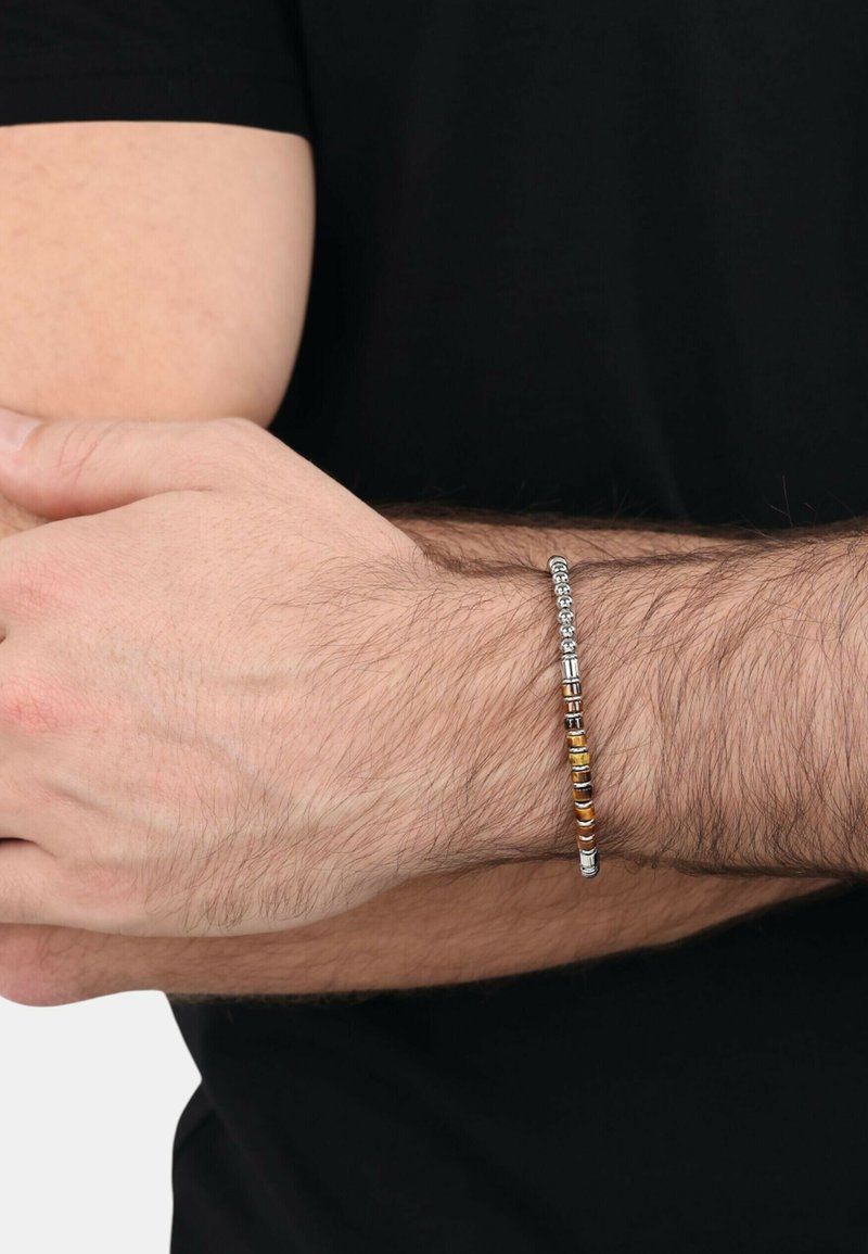 Bracciale in metallo caratterizzato da una combinazione di perle argentate e colorate con un design liscio e elegante. Indossato su un polso contro una t-shirt nera.