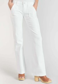 Pantalon large blanc avec poches avant, dot é d'une fermeture à bouton. Tissu texturé et ourlet droit. Associé à des sandales à plateforme marron.