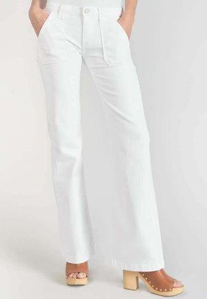 Pantalon large blanc avec poches avant, doté d'une fermeture à bouton. Tissu texturé et ourlet droit. Associé à des sandales à plateforme marron.