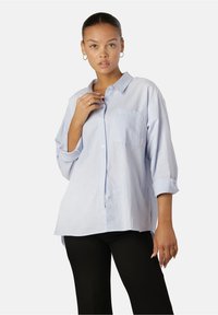Camicia button-up azzurro chiaro con taschino sul petto, maniche arrotolate e vestibilità rilassata. Realizzata in tessuto testurizzato, presenta dettagli di branding sottili.