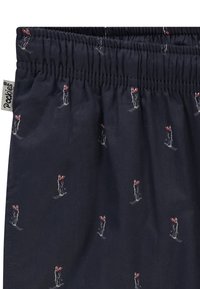 Marineblå shorts med elastisk midjebånd, med et gjentakende mønster av skiløpere i rødt og hvitt, laget av lett stoff.