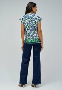 Top de manga corta con estampados en azul y verde sobre un fondo blanco, combinado con jeans de pierna ancha de color azul oscuro y tacones beige.
