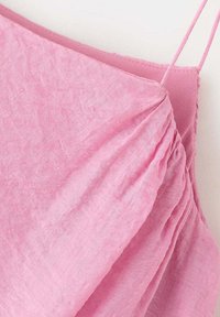 Gros plan d'une robe rose sans manches avec fines bretelles et des plis sur le corsage.