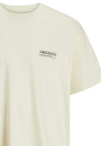 T-shirt à col rond à manches courtes en coton beige clair avec un logo vert "ORIGINALS JACK & JONES" imprimé sur la poitrine gauche.