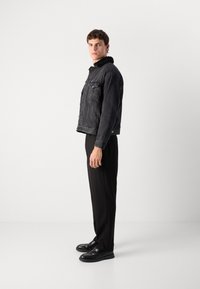 Chaqueta de mezclilla negra con un cuello de peluche, dos bolsillos frontales y un diseño corto, combinada con pantalones negros y zapatos negros.