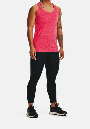 Uomo che indossa una canottiera sportiva rossa senza maniche, leggings aderenti neri e scarpe da corsa nere, in piedi contro uno sfondo semplice.