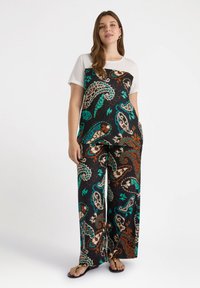 Mono de estampado paisley negro y multicolor con una parte superior blanca de manga corta, que cuenta con piernas anchas y bolsillos. Textura de tela suave.
