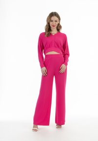 Completo due pezzi fucsia composto da un top cropped a maniche lunghe con scollatura rotonda e pantaloni a gamba larga. Tessuto morbido con una vestibilità rilassata.