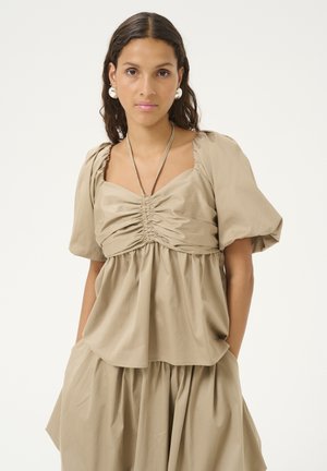 Beige pusero puff-sleeve, jossa on neliön muotoinen pääntie ja rypytyst yksityiskohtia edessä. Löysä istuvuus ja pehmeä kangas. Sisältää piilotetun taskun.
