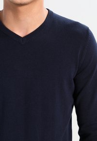 Mörkblå v-ringad tröja av stickat tyg, med ribbat krage och muddar, med en slät yta och långa ärmar.