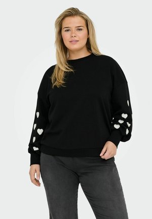 Sweatshirt noir avec des manches longues et surdimensionnées présentant des motifs de cœurs blancs. Texture lisse, col rond et taille ajustée.