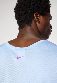 Hellblaues atmungsaktives Sportshirt mit Rundhalsausschnitt und lila Nike-Logo auf dem Rücken. Das Netzgewebe verbessert die Belüftung.