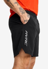 Svarta sportshorts med en lätt och slät textur, utrustade med sidokilar och en reflekterande "RVRC"-logotyp på vänster ben.