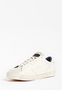 Baskets blanches à finition en daim, bout arrondi, lacets plats, accent noir sur la languette et motif triangulaire texturé sur le côté.