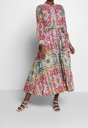Woman wearing a long-sleeve, collared, multicolored floral and geometric patterned maxi dress with white strappy heels.