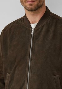 Braune Wildleder-Bomberjacke mit einem Reißverschluss vorne, geripptem Kragen und Seitentaschen. Die Textur ist weich mit einer glatten Oberfläche.