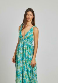 Długa, zwiewna sukienka z miękkiego materiału w wzór w odcieniach teal i aqua. Posiada głęboki dekolt w serek oraz pleciony detal w talii.