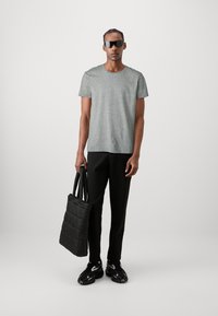 Gray crew-neck t-shirt, black tapered trousers, and black padded tote bag. Sporty black sneakers with reflective accents. Plain background.