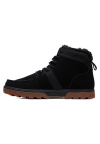 Black mid-top boots with suede and textile materials. Textured surface with a warm, fuzzy lining. Rubber sole with a brown traction pattern.