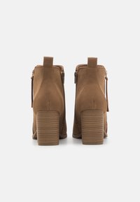 Brown suede ankle boots with a rounded toe, block heel, and side zippers. The heel features horizontal grooves for texture.