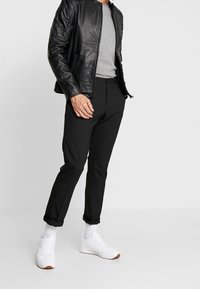 Giacca nera in pelle con zip sopra una maglietta grigia, abbinata a pantaloni neri slim-fit e sneaker bianche, con un design minimalista.