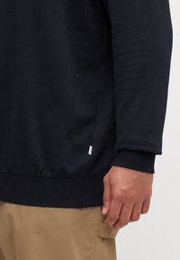 Granatowy sweatshirt z długimi rękawami, ściągaczami i zaokrąglonym dołem. Posiada małą metkę na bocznej szwie. Gładka tekstura bawełny.