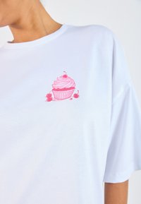 White cotton T-shirt featuring a pink cupcake graphic on the chest, with detailing of cream and cherries, in a relaxed fit design.