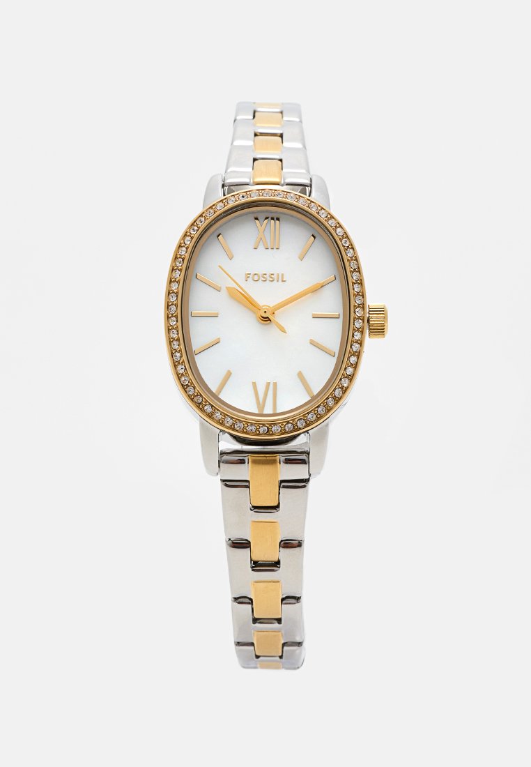 Montre pour femmes Fossil au design ovale, bracelet en métal argenté et doré, cadran blanc et lunette en cristal étincelant. Index et aiguilles dorés.