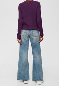 Fialový žebrovaný pletený svetr v kombinaci se světle modrými širokými džínami. Má dlouhé rukávy a kulatý výstřih.